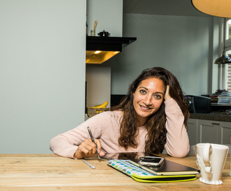 Vrouw aan keukentafel met notitieboekje en telefoon